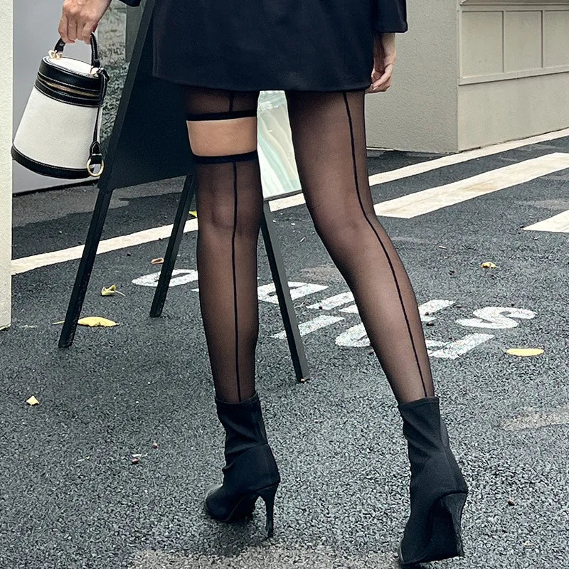 Person wearing black sheer stockings and high-heeled shoes on a street.